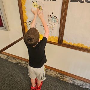 Pre-school aged boy hangs up a paper bee he colored in a display case to show his participation in the library's 1000 Books Before Kindergarten reading challenge
