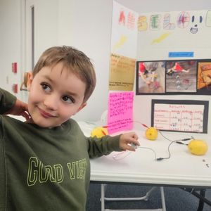 child holds a small digital watch face that is connected to a network of lemons by wire
