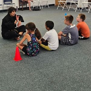 group of children sit politely listening to a black belt martial arts teacher speak about Tang Soo Do Korean karate