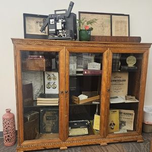 A display cabinet show a variety of old and vintage library materials like a movie projector, type writer, WWII era tin of crackers, local yearbooks, framed photos of Greensburg storefronts, a card catalog drawer, etc.