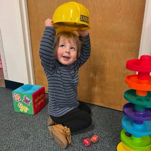 toddler puts on yellow hard hat while playing