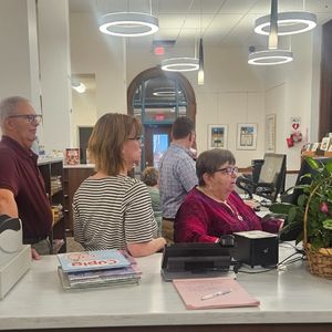 Library staff stand behind the circulation desk receiving instruction on how to use the new check out system and practice on the computers
