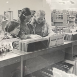 Photo of a woman, teen girls and young girl looking at records to listen to inside the library during the 1960s and 70s